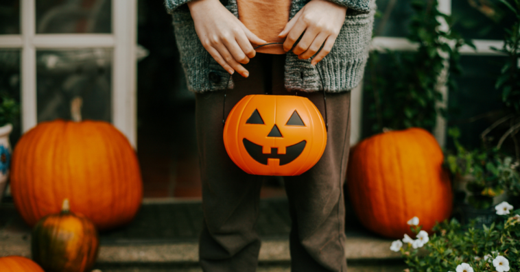 A child holding a jack o'lantern shaped trick or treating bag.