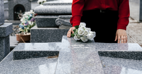 A woman placing a white rose on a grave.