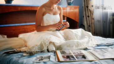 bride seated on bed in wedding dress going through photographs