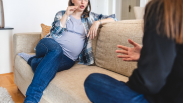 angry pregnant person seated on couch speaking to someone