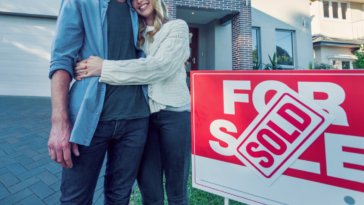 couple pose by sold sign in front of house