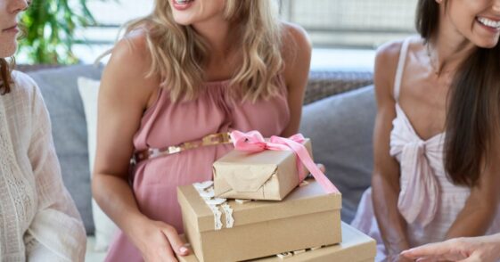 Pregnant woman holding gift boxes by friends at baby shower.