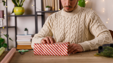 a man in a white sweater wrapping a christmas gift