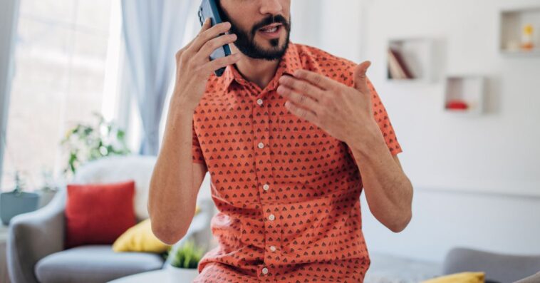 One man, talking on mobile phone in living room at home.