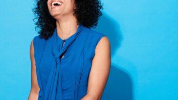 Close-up of a woman laughing and smiling against a blue background.