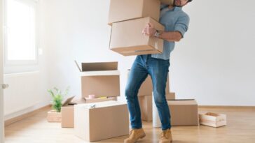 Young man clumsy carrying a stack of cardboard boxes while moving into an new apartment.