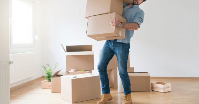 Young man clumsy carrying a stack of cardboard boxes while moving into an new apartment.