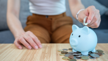 A woman putting a coin in a piggy bank.