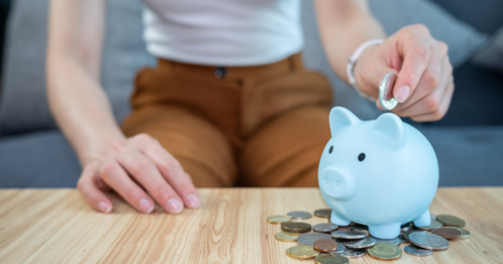 A woman putting a coin in a piggy bank.