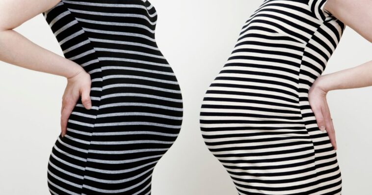 Two pregnant women in striped dresses face one another, stomach to stomach.