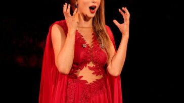 Taylor Swift, wearing a red dress, stands in stage with a look of great joy.