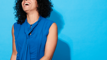 A woman laughing in front of a blue background.