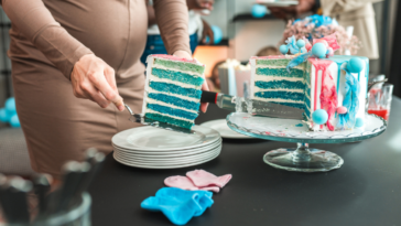 A pregnant woman cutting into a blue cake.