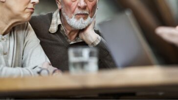 Worried mature couple talking to insurance agent at home.