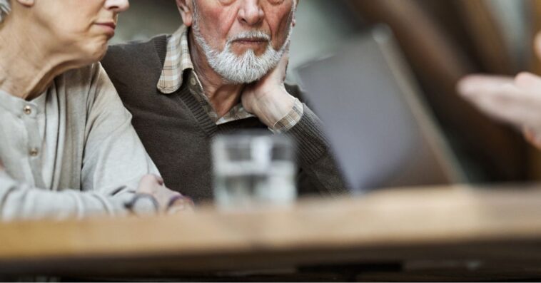 Worried mature couple talking to insurance agent at home.