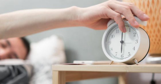 A man hitting the snooze button on his alarm clock.