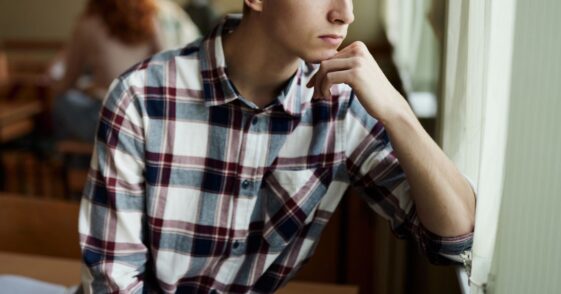 Lonely high school student, male, feeling excluded while looking through window during a break in the classroom.