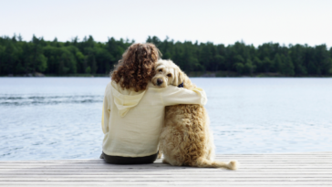 A woman sitting on a dock, hugging her dog.