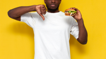 man giving thumbs down sign while holding hamburger