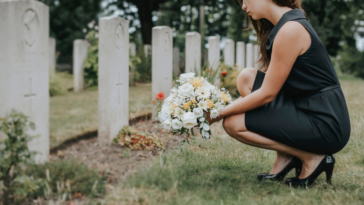 woman laying flowers on a grave in cemetery