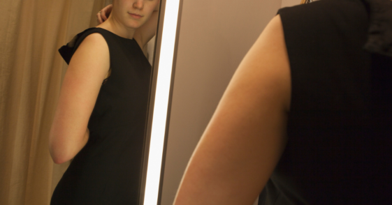 young woman trying on dress in front of mirror