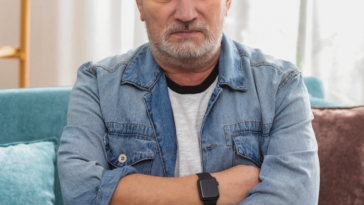 An older man sitting on the sofa with his arms crossed.