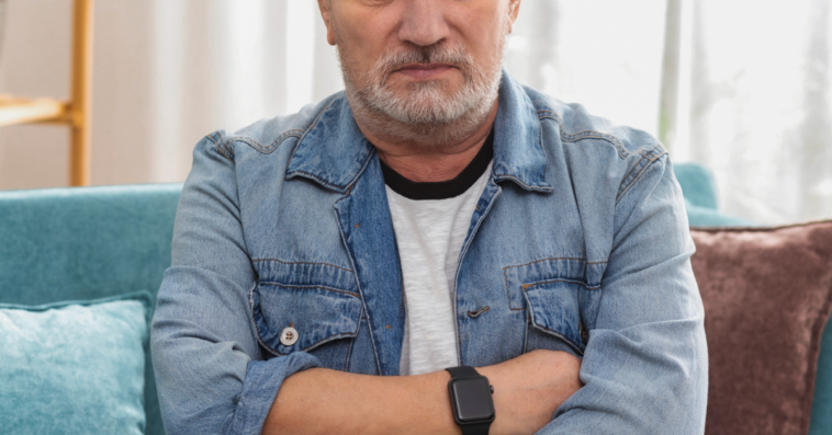 An older man sitting on the sofa with his arms crossed.