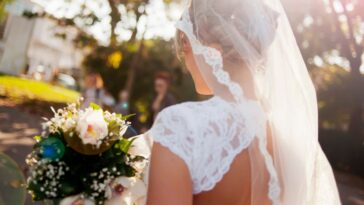 Beautiful bride holding flower bouquet view from back, lens flare.