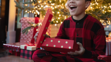 A boy sitting in front of a Christmas tree holding a Christmas present.