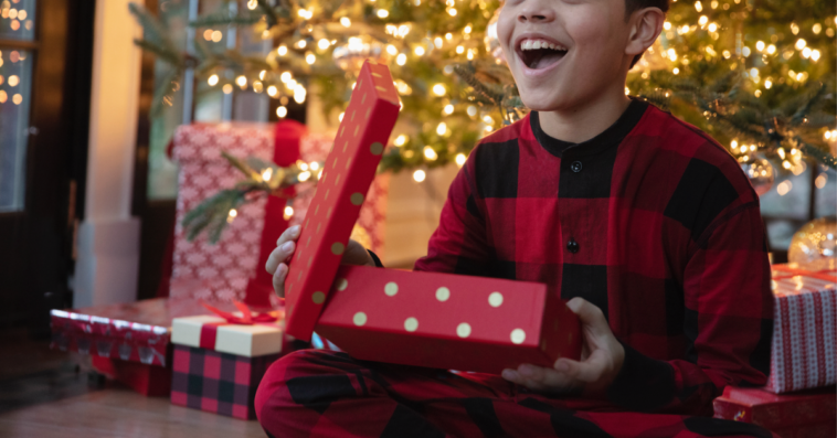 A boy sitting in front of a Christmas tree holding a Christmas present.