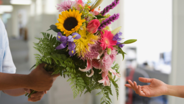 A woman in an office behing handed a bouquet of flowers.