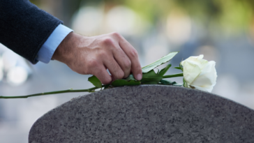 A man laying a flower on a gravestone.