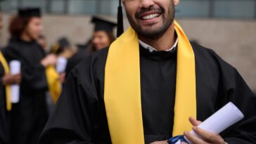 Portrait of a happy graduate student holding his diploma on graduation day and looking at the camera smiling.