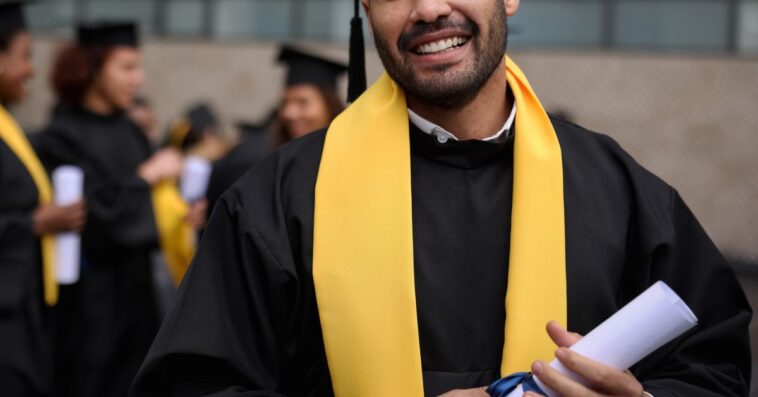 Portrait of a happy graduate student holding his diploma on graduation day and looking at the camera smiling.