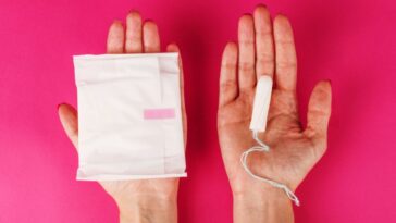 Woman holding menstrual tampon on a pink background.