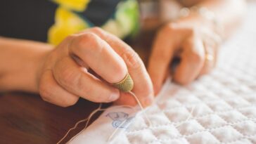 Cropped view of woman sewing a hem on a quilt.