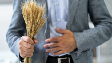 A man holding a pile of wheat with his other hand on his stomach.