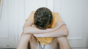 A teenage boy sitting on the floor with his head in his hands.