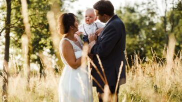 Bride and bridegroom with toddler amidst plants on field.