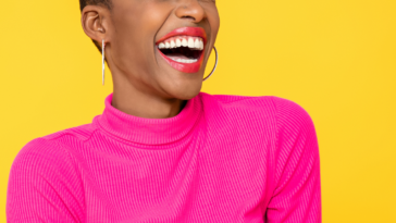 A woman wearing a pink shirt laughing in front of an orange background.