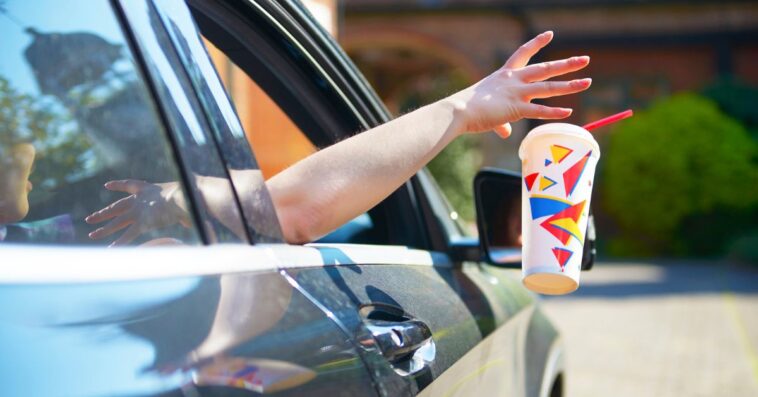 Person discarding a soft drink cup out car window