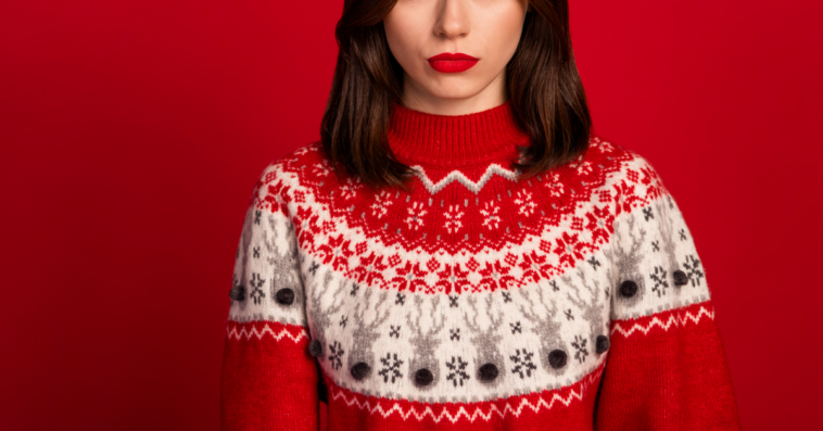 A woman frowning in an ugly Christmas sweater.