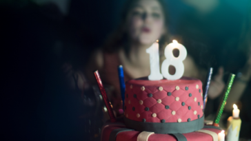 A girl blowing out candles on a cake with the number 18 on the top