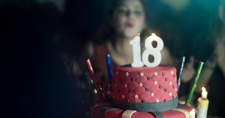 A girl blowing out candles on a cake with the number 18 on the top