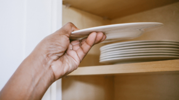 A man putting a plate away on a high cupboard.