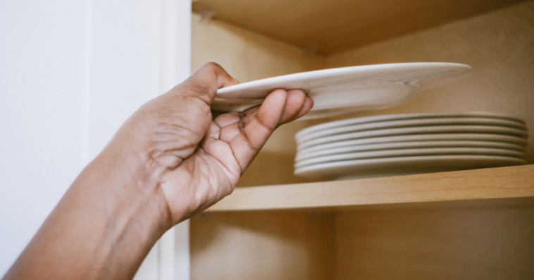 A man putting a plate away on a high cupboard.