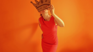 A woman holding a paper mask in front of her face.