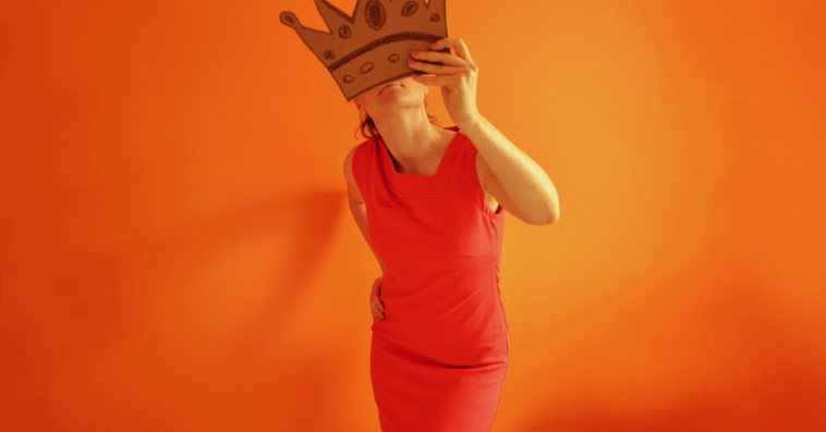 A woman holding a paper mask in front of her face.