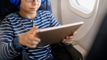 young boy seated on airplane looking at tablet