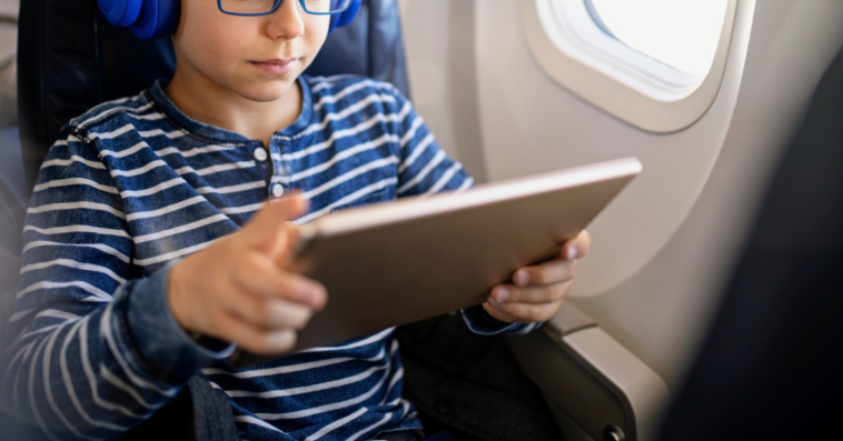 young boy seated on airplane looking at tablet